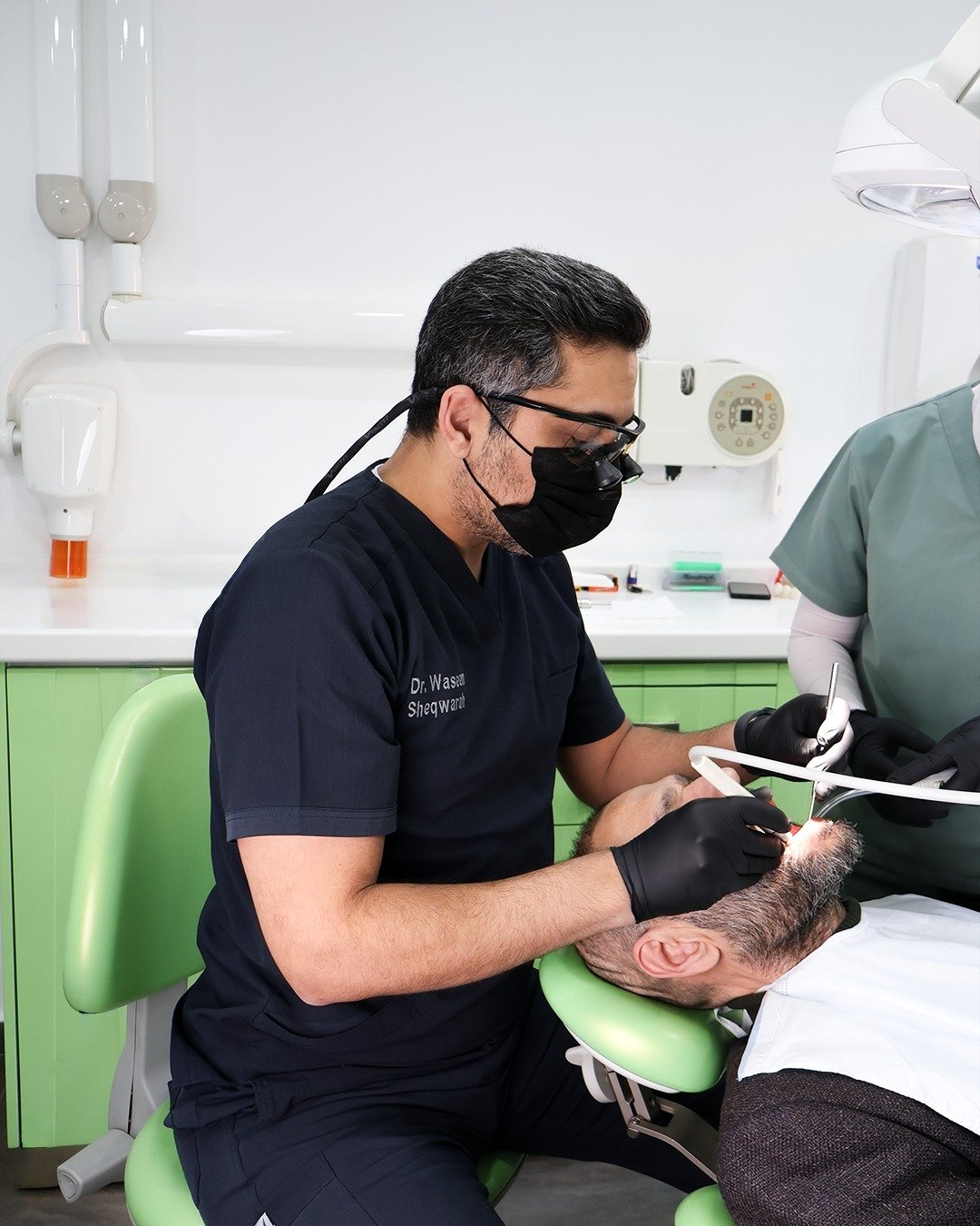 Dr. Waseem Sheqwarah treating a patient at his clinic in Amman, wearing magnification loupes